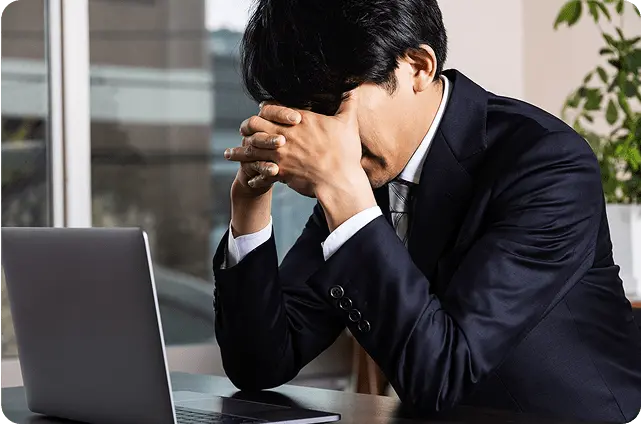 パソコンの前で頭を抱えて悩んでいるスーツ姿の男性